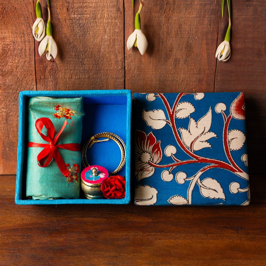 Kalamkari-covered wedding seer box holding folded silk, gold bangles and a brass kumkum holder